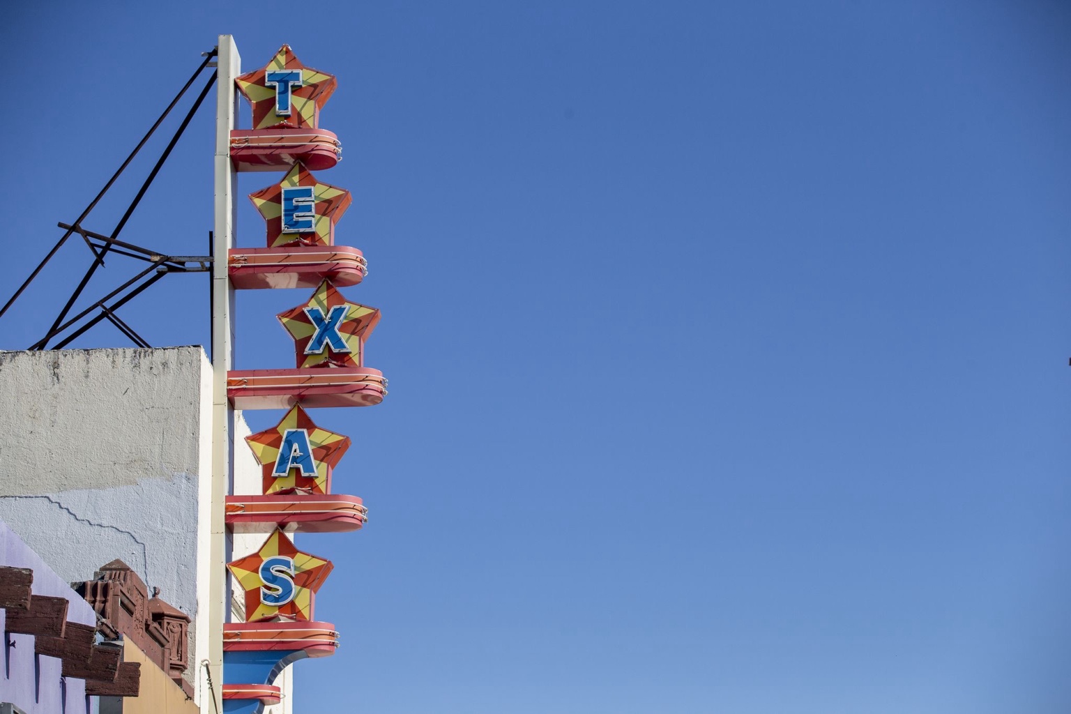 The Texas Theatre’s vertical TEXAS sign with colorful stars and curved red neon bands against a blue sky